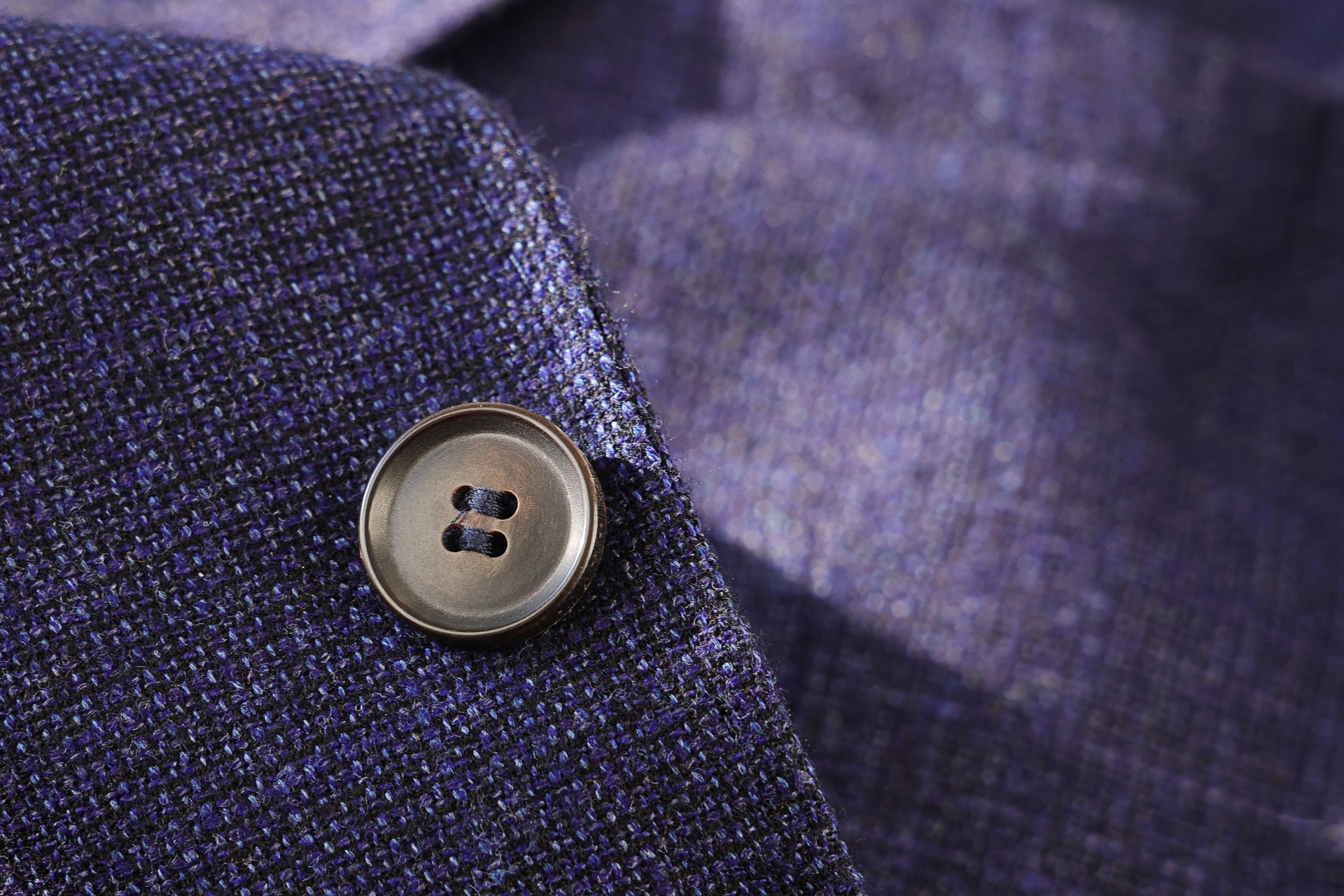 A detailed, close-up shot of a single button on a dark purple-blue tweed blazer.